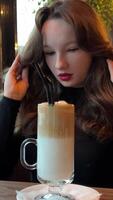Side view of woman in pajamas drinking coffee in morning and looking out window, slow motion. Greenery on background. Girl relaxing and enjoying video
