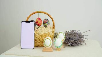 Easter basket with eggs and a green screen phone on a white background. Chroma key vertical smartphone mock up for advertising on the eve for the Christian holiday video