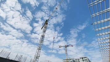 Two tall cranes on a construction site, viewed from below. Cloudy sky background video