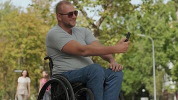 Man in a wheelchair talking on the phone during a break in the park. video