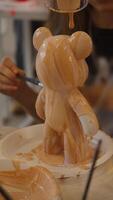 In the manual production of children's toys, a teddy bear figurine is watered with viscous epoxy paint to create a unique color and pattern. video
