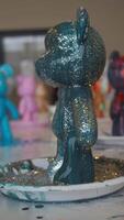 A close-up of a teddy bear figurine, painted with epoxy paint and covered in glitter, during a workshop for creating children's toys. Vertical. video
