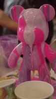 With the help of a brush, the artist creates an abstract drawing using viscous pink paints that flow from the figurine of a bear cub. video