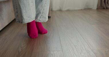 young woman joyfully jumps and walks away showcasing her bright pink socks Dressed in casual jeans she moves dynamically across a light wooden floor in a cozy indoors setting video