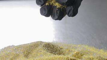 Black gloved hand dropping golden diamond abrasive powder onto a reflective surface, Macro view of controlled material handling during tool production preparation video