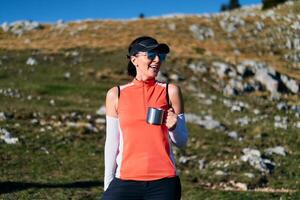 A female hiker enjoys a warm cup of tea while resting after a challenging mountain climb.A woman hiker takes a peaceful break, sipping tea and enjoying the view after a strenuous mountain climb photo