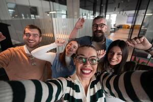 A diverse group of business professionals take a break from their tasks in a modern startup open space modern office to capture a creative selfie, showcasing teamwork and a vibrant workplace culture. photo
