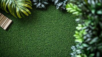 Overhead view of a lush, green artificial turf surface bordered by leafy plants and a small wooden slat structure. High-angle shot. photo