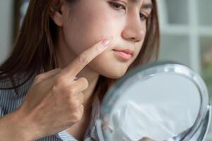 Self-Reflection and Skin Assessment. Pointing to a blemish while looking in the mirror. photo