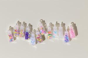 Set color glitters for nail art and makeup in glass jars on beige background. Trend Flat lay with glitter for nails in bottles with sahdows and glare, visual for manicure, creative layout photo