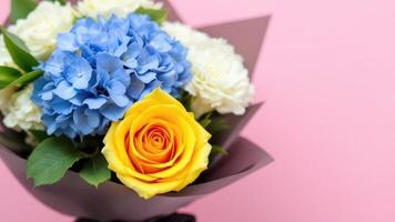 Vibrant Bouquet of Blue, Yellow, and White Flowers in Black Wrapping on Pink Background photo