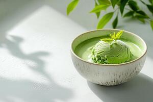 Matcha ice cream served in a rustic bowl next to fresh green leaves in soft sunlight. creamy scoop of matcha ice cream rests in a rustic bowl on clean background, surrounded by vibrant green leaves photo