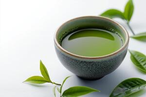 Discovering the vibrant elegance of matcha tea in a traditional bowl surrounded by fresh green leaves. rustic bowl filled with rich green matcha tea on smooth surface, accompanied by fresh tea leaves photo