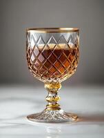 Elegant crystal glass filled with rich brown liquid on a marble surface in soft lighting. Crystal glass filled with cognac on a smooth marble surface, showcasing a rich brown liquid, luxurious feel photo