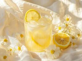 Refreshing lemon drink with ice and flowers on a soft surface photo
