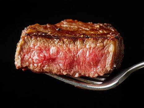 Juicy grilled steak served on a fork in a dark setting photo