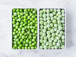 Fresh and frozen green peas in contrasting trays on a marble surface photo