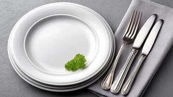 Elegant white plate set on a dining table surrounded by blurred utensils and napkin in an inviting meal setting. Clean white plate on a dining table, complemented by blurred silver utensils photo