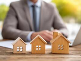 Real estate agent focused on laptop at modern workspace with wooden home models and contract documents. Real estate agent is diligently working on a laptop at a pro desk filled with wooden home models photo