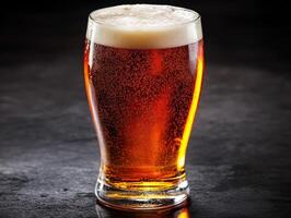 Sparkling amber beer in a clear glass container on dark surface photo