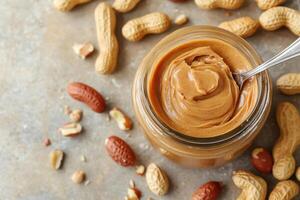 Smooth peanut butter in jar surrounded by peanuts on table photo