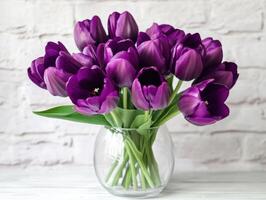 Purple tulips in a clear vase on a light brick background photo