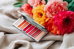 Blush palette featuring coral and peach tones alongside vibrant fresh flowers on soft linen with natural sunlight illuminating the scene. blush palette in coral and peach tones on soft linen fabric photo