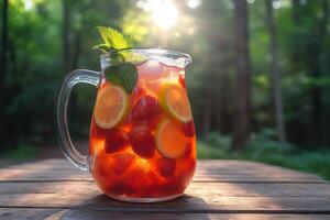 Refreshing strawberry lemonade in glass pitcher on wooden table in forest setting photo