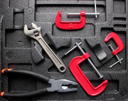 Pliers, adjustable wrench and different thread clamps in styrofoam compartments case top view photo