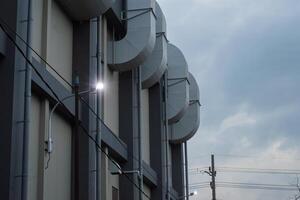The modern factory building with large ventilation looks majestic under the evening cloudy sky. Pipes and electrical wiring complete the industrial look, creating a futuristic and rugged atmosphere. photo