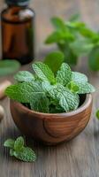 Fresh mint leaves in a wooden bowl on a rustic table with a background of herbs and essential oil bottle photo