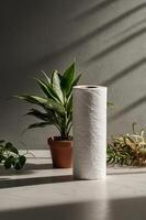 White paper roll stands next to green plants in a sunlit indoor space with soft shadows creating a serene atmosphere photo
