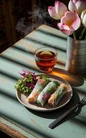 spring rolls is accompanied by a small side of mixed greens and a steaming cup of tea on a wooden table photo