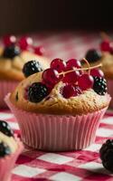 A delightful muffin topped with fresh red currants and blackberries sits on a red and white checkered tablecloth. photo