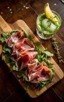 Delicate slices of prosciutto are artfully arranged on a bed of fresh greens, served on a wooden board photo