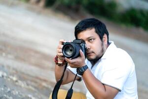 Professional Asian beard - mustache Camera man 2posture and focus in viewfinder and LED screen on mirrorless camera medium format in construction concrete area. photo