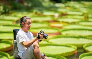 Asian Man is holding a camera and taking a photo at outdoor field with the Lily Lotus Leaf pond background.11