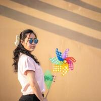 Asian woman posts and play Windmill Toy colourful rainbow colour on the building rooftop in sunset time.5 photo