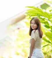 Asian woman looks at Cameraa, Stands and posts with shy, pretty smile and happiness photo