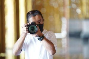A man wearing black mask is shooting photo through a viewfinder camera with the right eye.1
