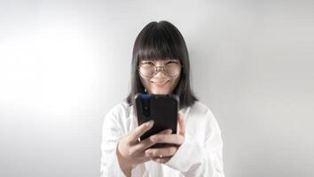 Isolated Pretty Asian glasses woman looks at camera a1nd holds mobile phone in her hand on white background in studio light. photo