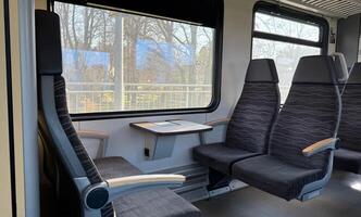 Modern Train Interior with Comfortable Seating and Large Windows. Spacious and inviting modern train interior featuring upholstered seating, accessible table space, and panoramic windows providing ample natural light with views of the outside landscape. photo