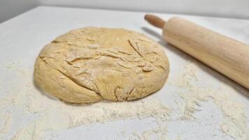 Fresh Dough Ready for Baking with a Rolling Pin and Flour Dusting. Raw dough ball on a floured surface, accompanied by a wooden rolling pin, set for baking preparations. Captures the essence of baking creativity and culinary inspiration. photo