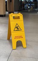 Bright Yellow Caution Warning Sign Indicating Slippery Conditions in Modern Indoor Space. A yellow caution sign on a tiled floor indicating a slippery surface, located indoors with a modern background photo