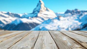 Rustic wooden table with blurred view of snowy mountain peak and alpine architecture, crisp morning light enhances cool tones. photo