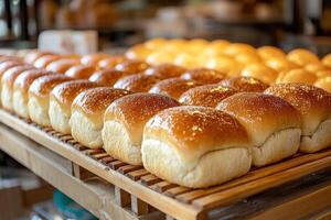 Freshly baked artisanal bread rolls arranged neatly on wooden rack, showcasing their golden crust and soft texture in warm bakery setting photo