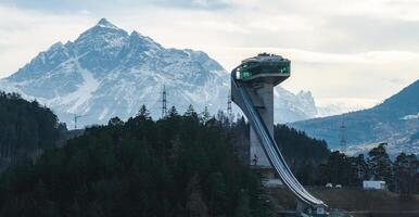 The Bergisel Ski Jump in Innsbruck, Austria, features modern architecture, dense forests, and snow capped Alpine peaks in the background. photo