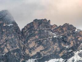 Rugged peaks in the Dolomites, Italy, with warm orange and gray tones, partial snow cover, and clouds hovering near the sharp formations. photo
