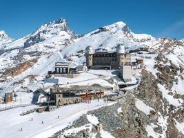 Aerial view of Gornergrat Observatory in Zermatt, Switzerland, with twin domes, snow covered Alps, Matterhorn peak, train station, and visitors below. photo