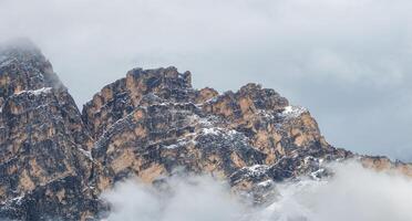 Rugged mountain peaks in the Dolomites, Italy, partially covered in mist and snow. Light and shadow highlight the jagged texture of the rocky formations. photo